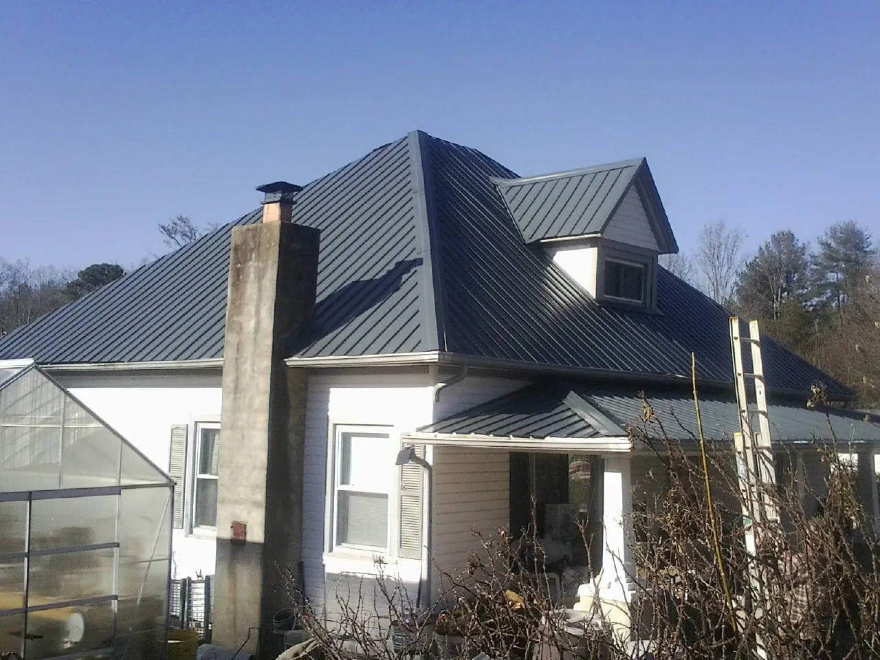Dark blue standing seam metal roof on a white farmhouse with dormer — Slate & Tile Roof Repair by Roofing Brothers in Breezy Point