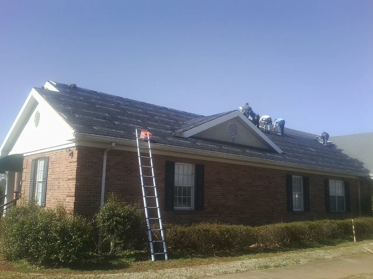 Crew tearing shingles off a brick ranch roof with a ladder set — Metal Roof Repair work by our crew in Breezy Point