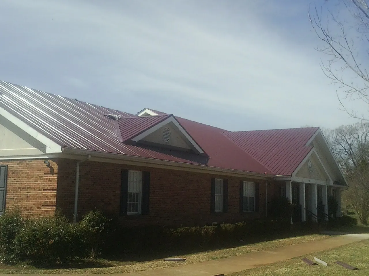 Red metal roof with gabled entries on a long brick building, from a Hail Damage Roof Repair job in Breezy Point