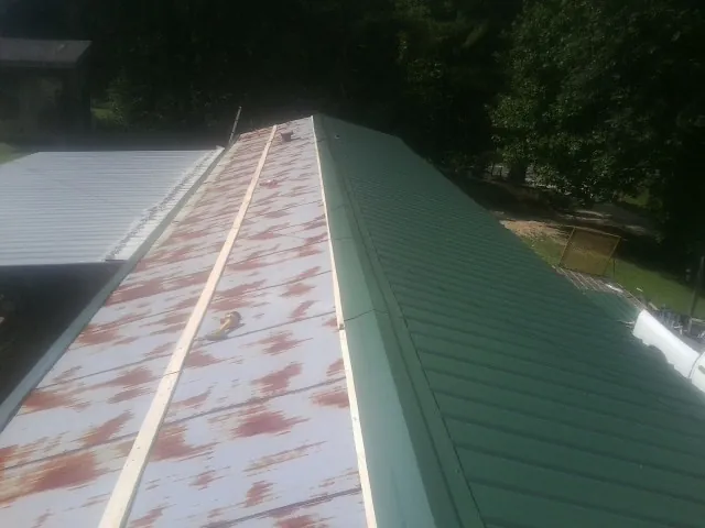 Old rusted panels beside newly installed green metal roofing — Wind Damage Roof Repair by Roofing Brothers in Breezy Point