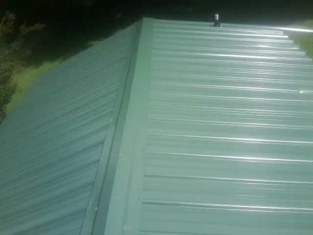 New green metal panels meeting at the ridge of a roof — Flat Roof Repair work by our crew in Breezy Point