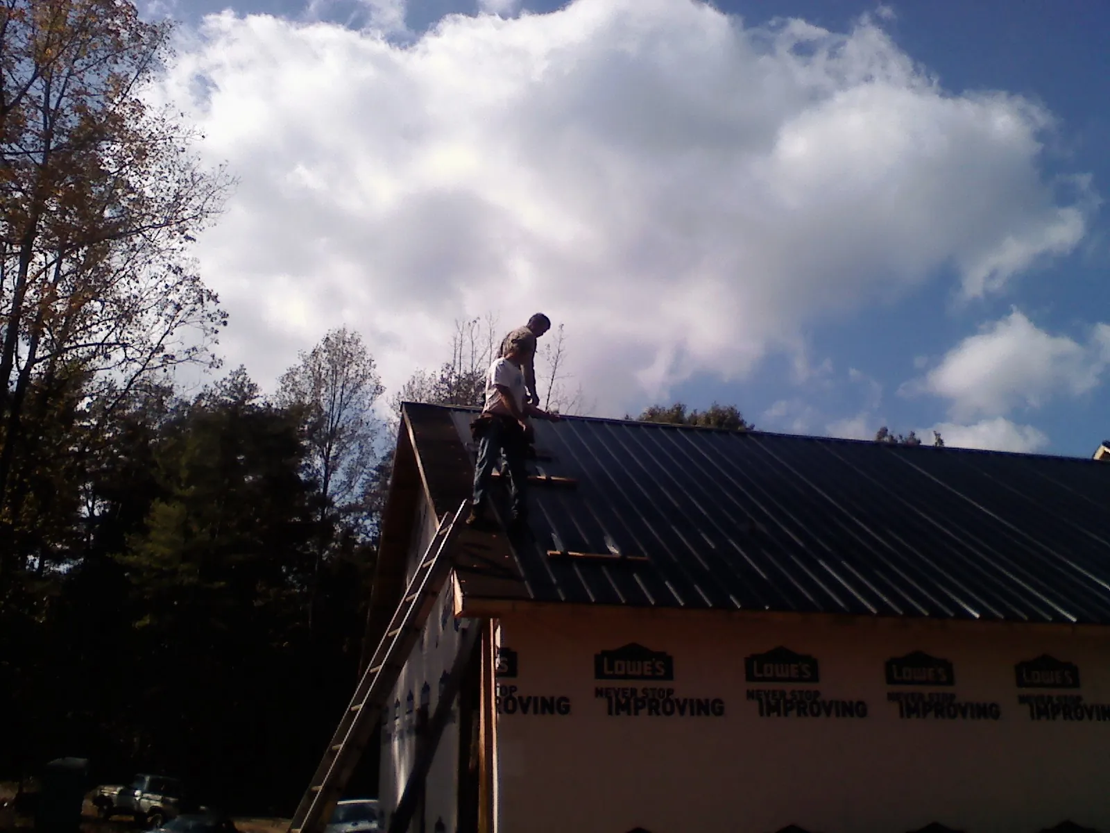 Roofer fastening dark metal panels high against a cloudy sky, from a Roof Inspection job in Breezy Point