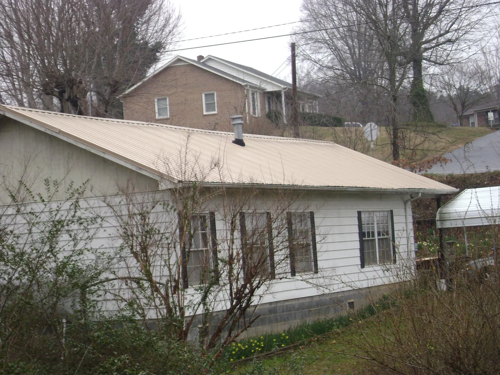 Tan metal roof on a white sided house set into a hillside — Commercial Roofing by Roofing Brothers in Breezy Point