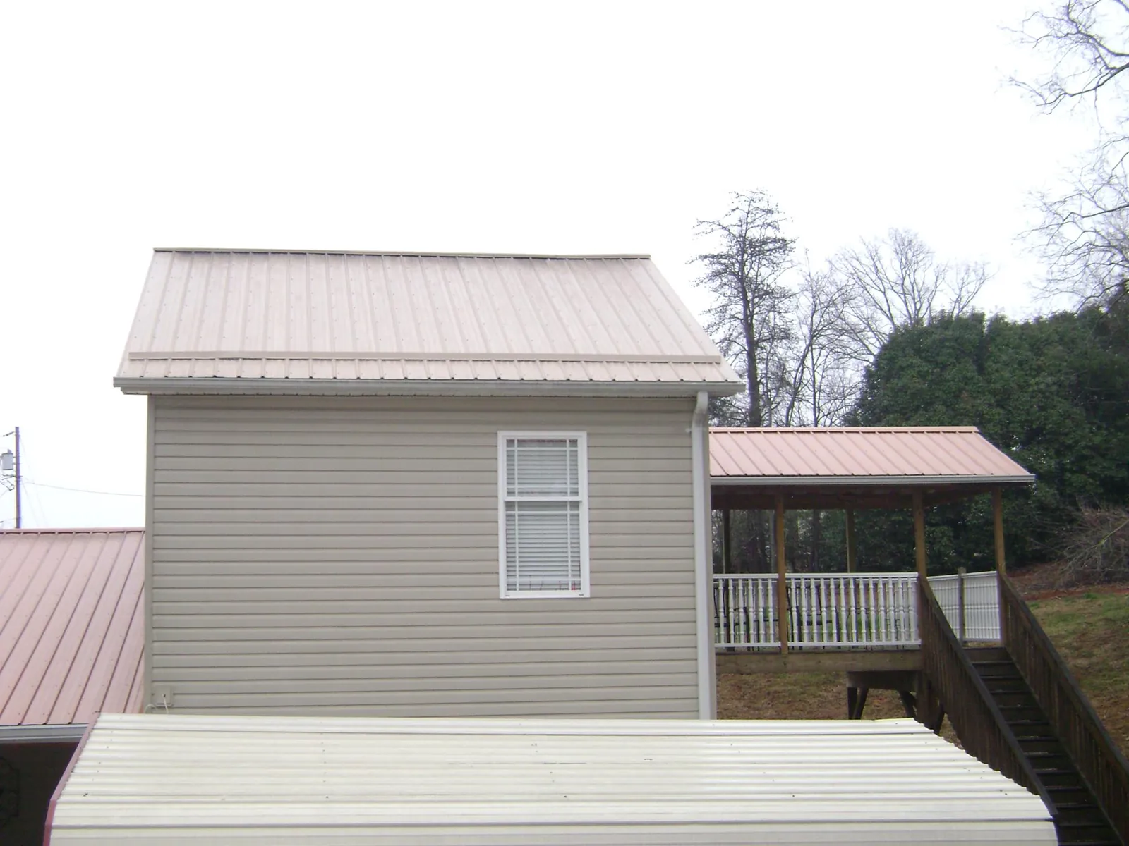 Tan metal roofs on a two story addition and attached porch, from a Roof Replacement job in Breezy Point