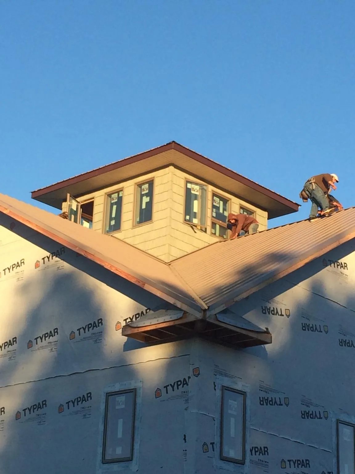 Roofers working around a rooftop cupola on a new metal roof at sunset — Roof Waterproofing in Breezy Point by Roofing Brothers